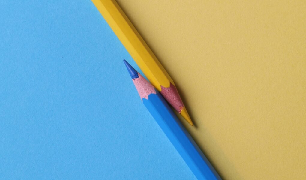 Close-up of vibrant yellow and blue colored pencils on contrasting paper backgrounds.