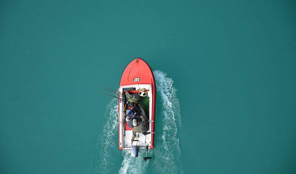 Top view of a red motorboat with fishermen navigating open turquoise waters.