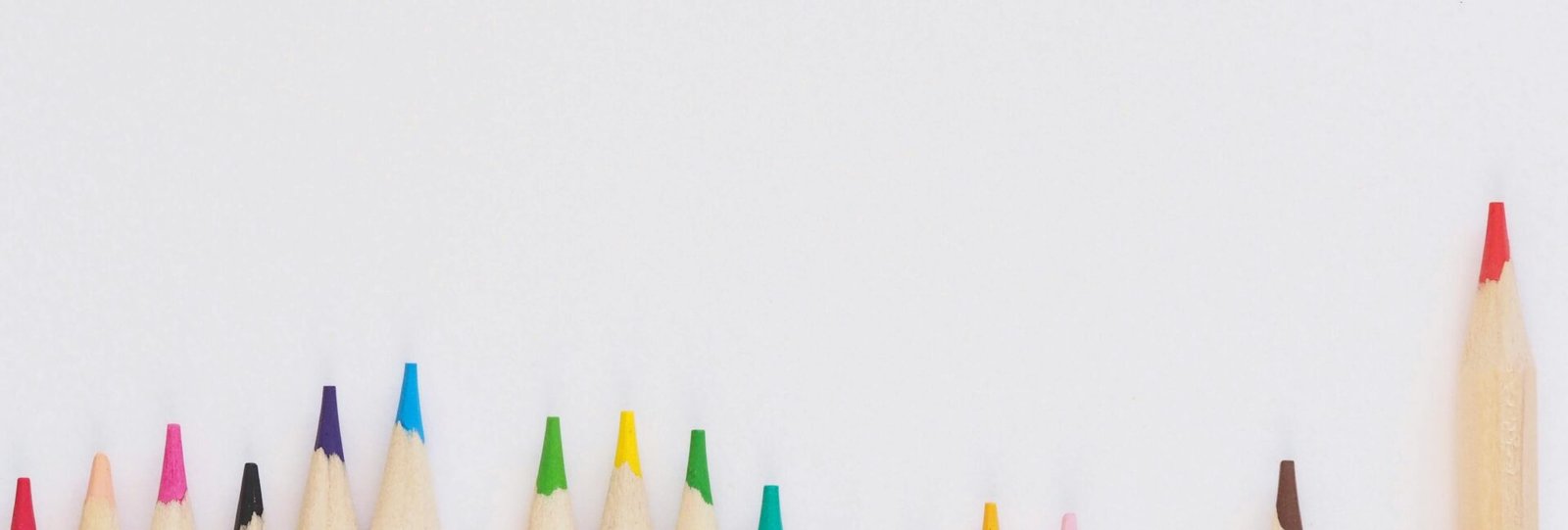 A row of vibrant colored pencils aligned on a white background, providing ample copyspace.