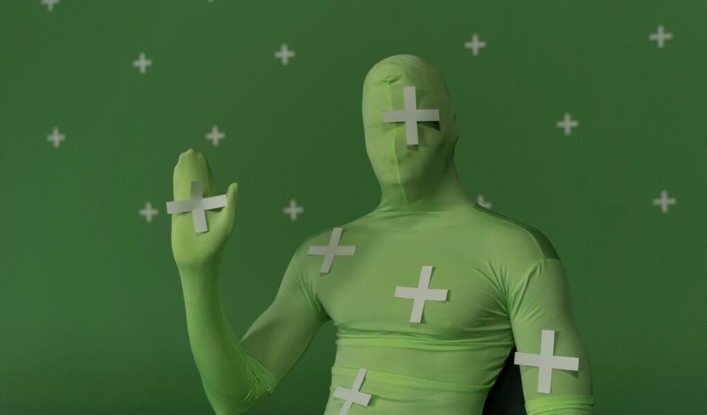 Person wearing a green screen suit with tracking markers for visual effects work.